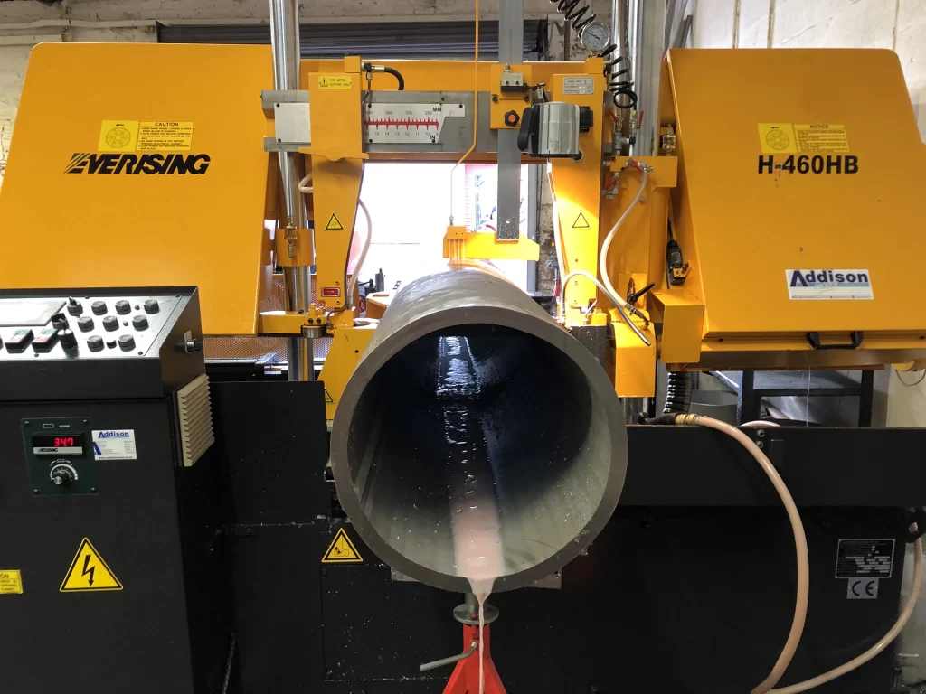 Home 1 Cut-to-length stainless steel pipe being cut on a bandsaw